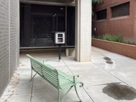 A green bench next to a building and a Little Free Library.