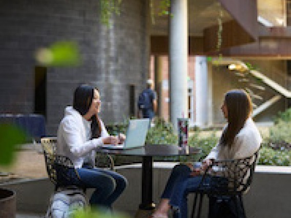 two students with laptops sitting at a table in an outdoor courtyard