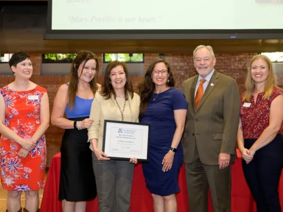 Six people smiling at the camera, one holding an award in the center