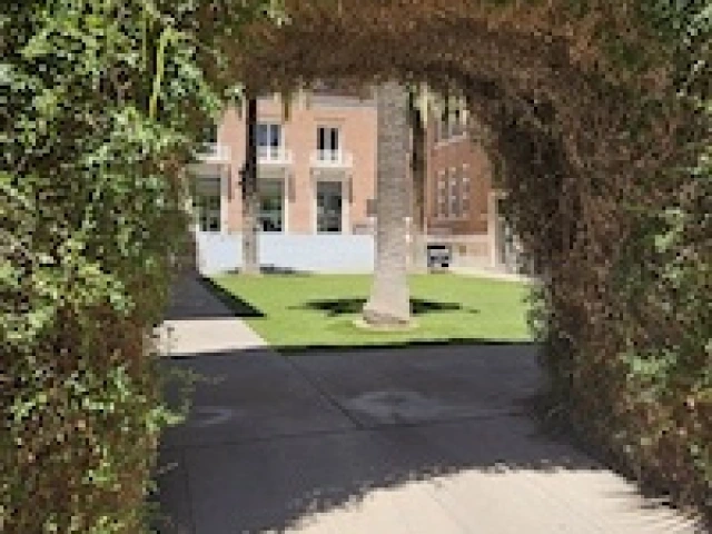 Vines cover an arched pathway into a grassy courtyard of a brick building.