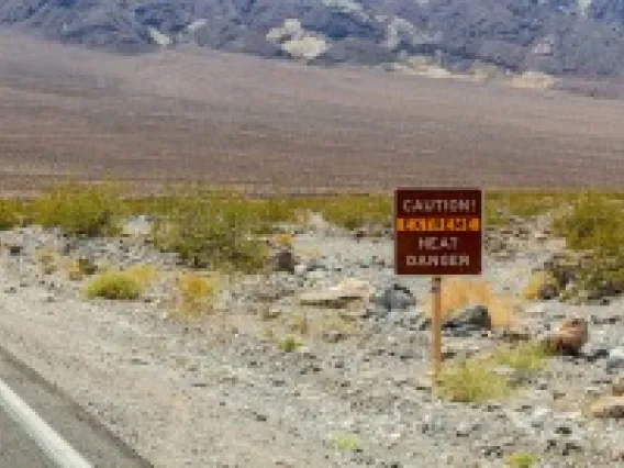 a sign that says "caution extreme heat danger" next to a road in a desert