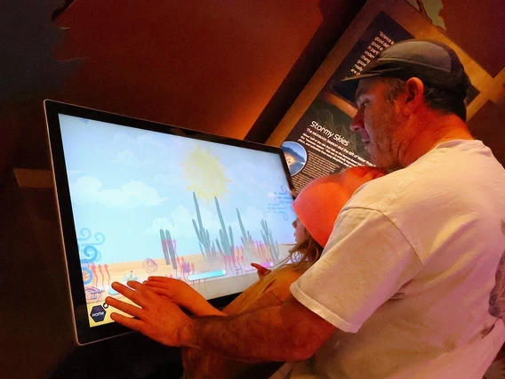 a man looking at an interactive screen in a museum with his child