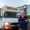 Bill Mason standing outside a Cat Tran shuttle near a building in the background with a Block A logo on it